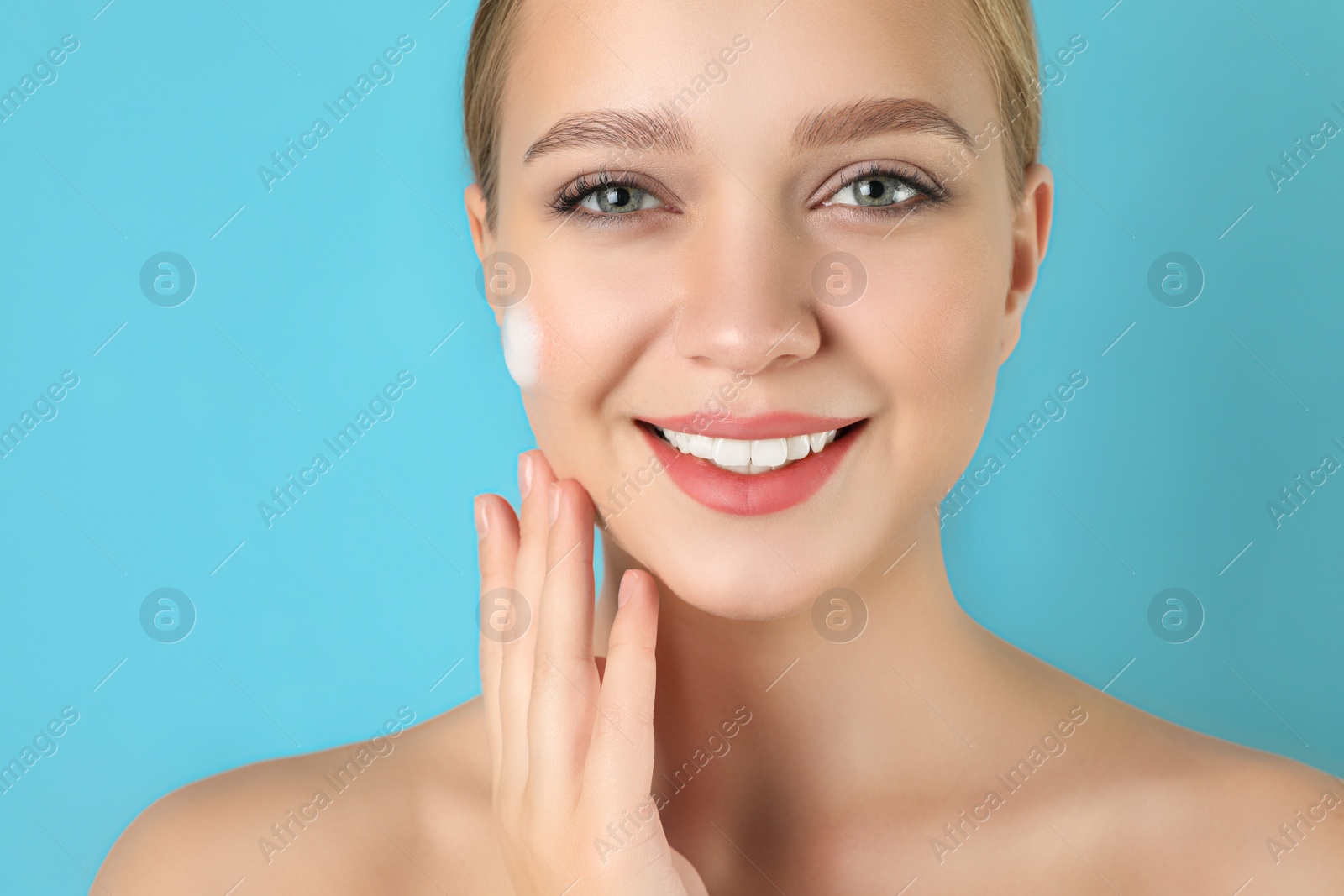 Photo of Young woman washing face with cleansing foam on light blue background. Cosmetic product