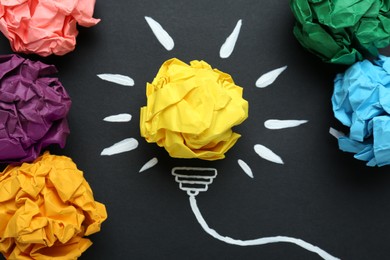 Photo of Flat lay composition with yellow crumpled paper ball and drawing of lamp bulb on blackboard. Idea concept