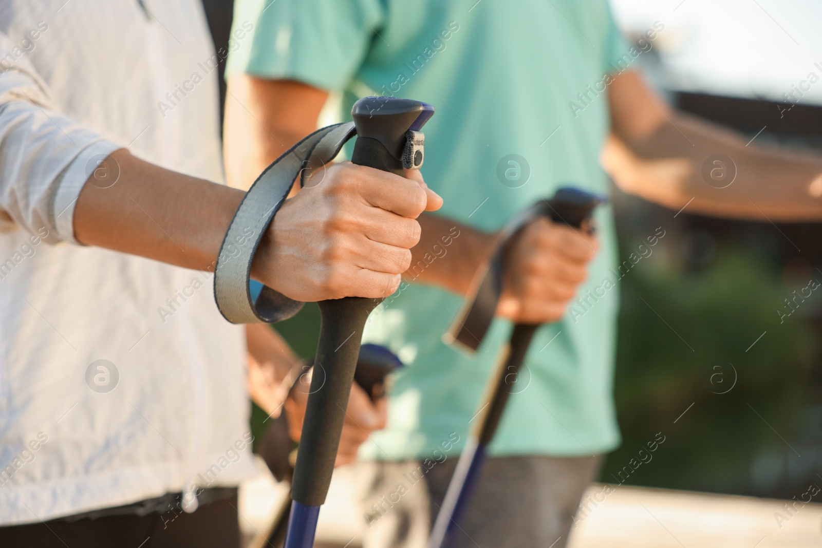 Photo of Couple practicing Nordic walking with poles outdoors, closeup