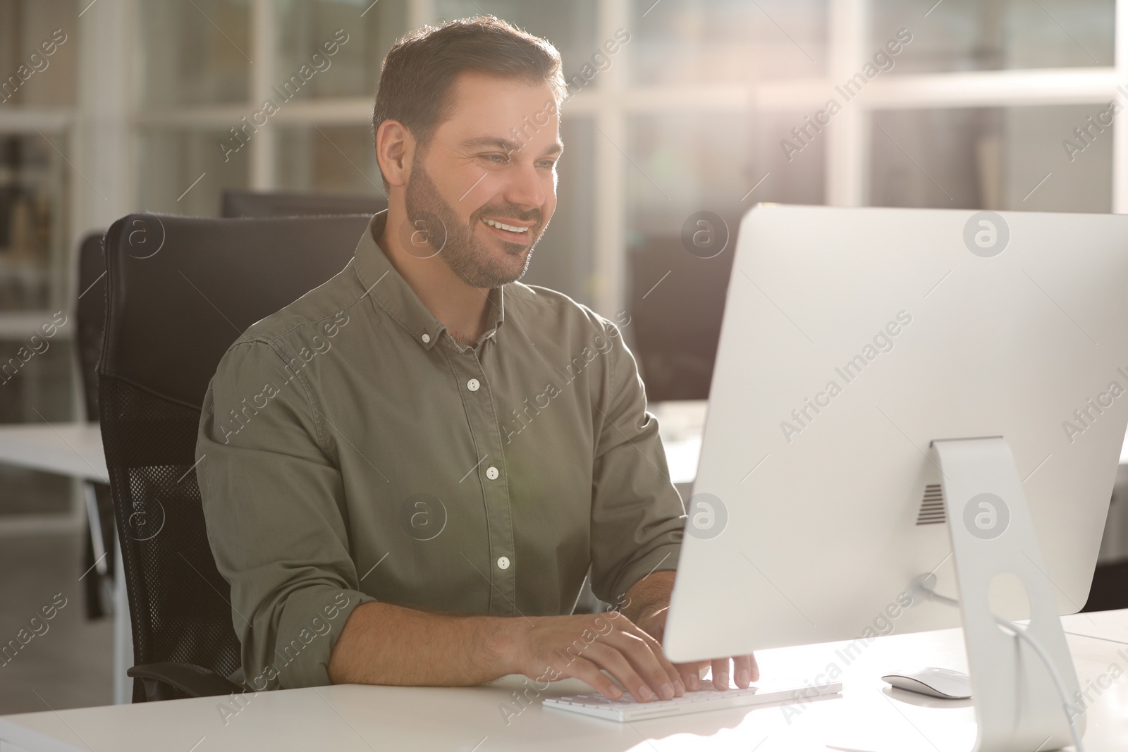 Photo of Happy man using modern computer at white desk in office