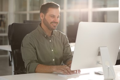 Happy man using modern computer at white desk in office