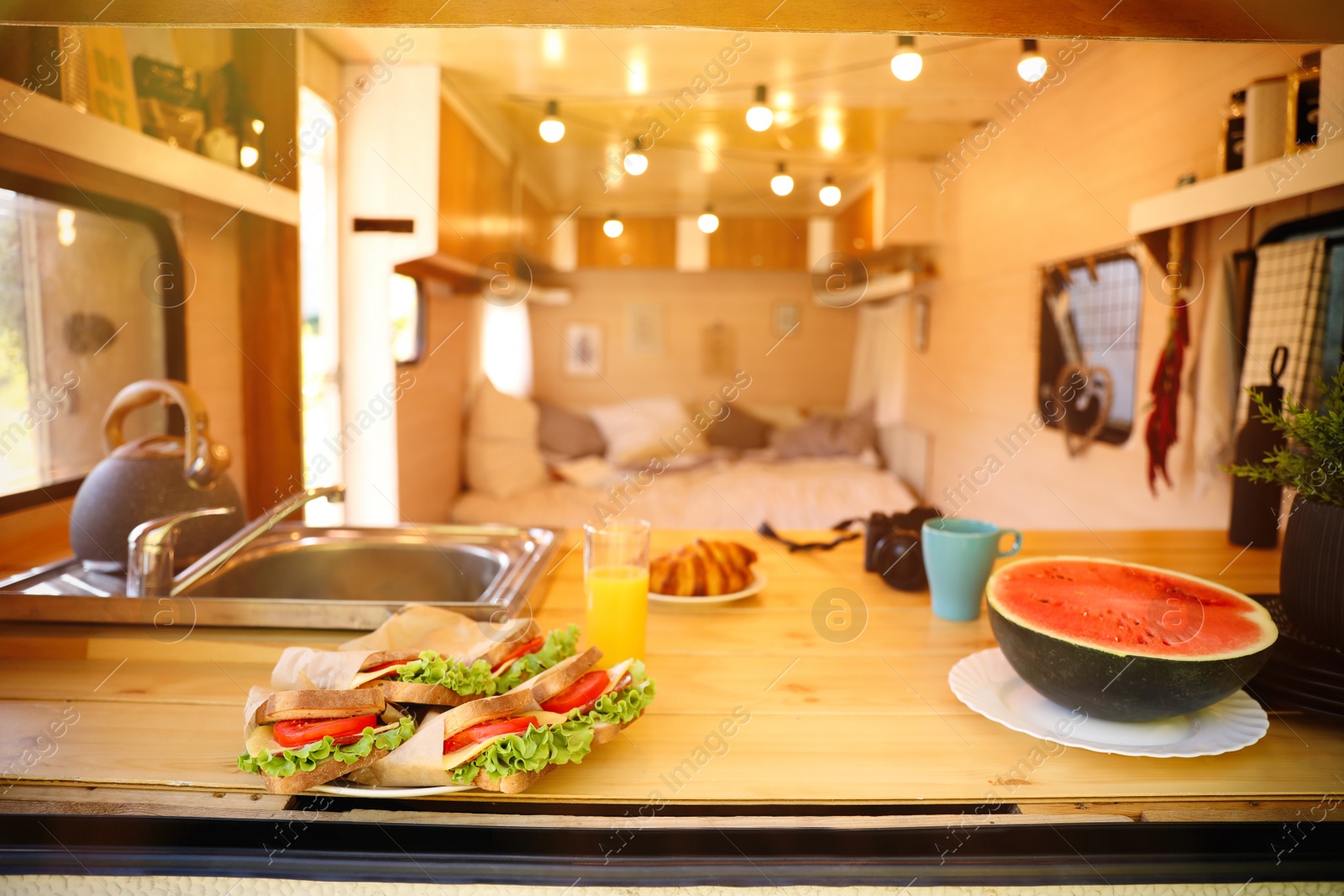 Photo of Delicious sandwiches and watermelon on wooden table in modern trailer. Camping vacation