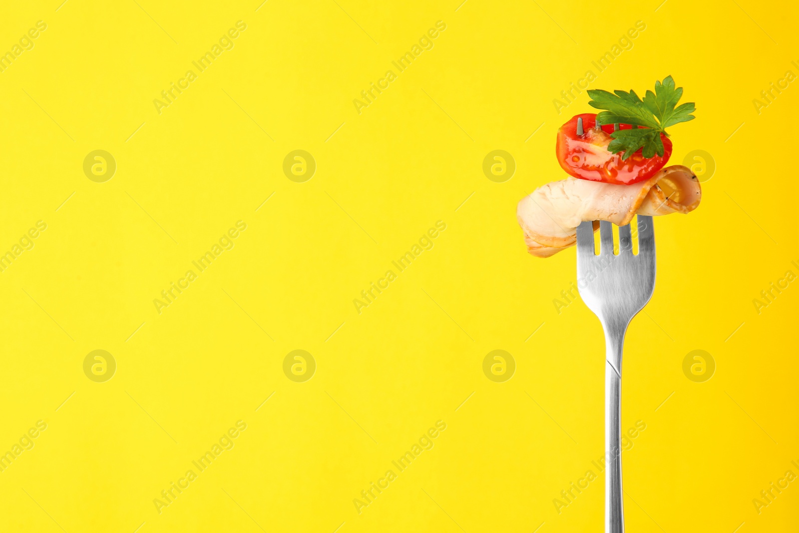 Photo of Fork with slice of ham, cut tomato and parsley on yellow background, space for text