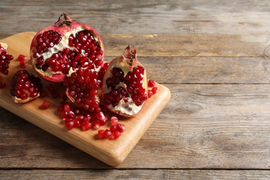 Photo of Board with ripe pomegranates and seeds on wooden background, space for text