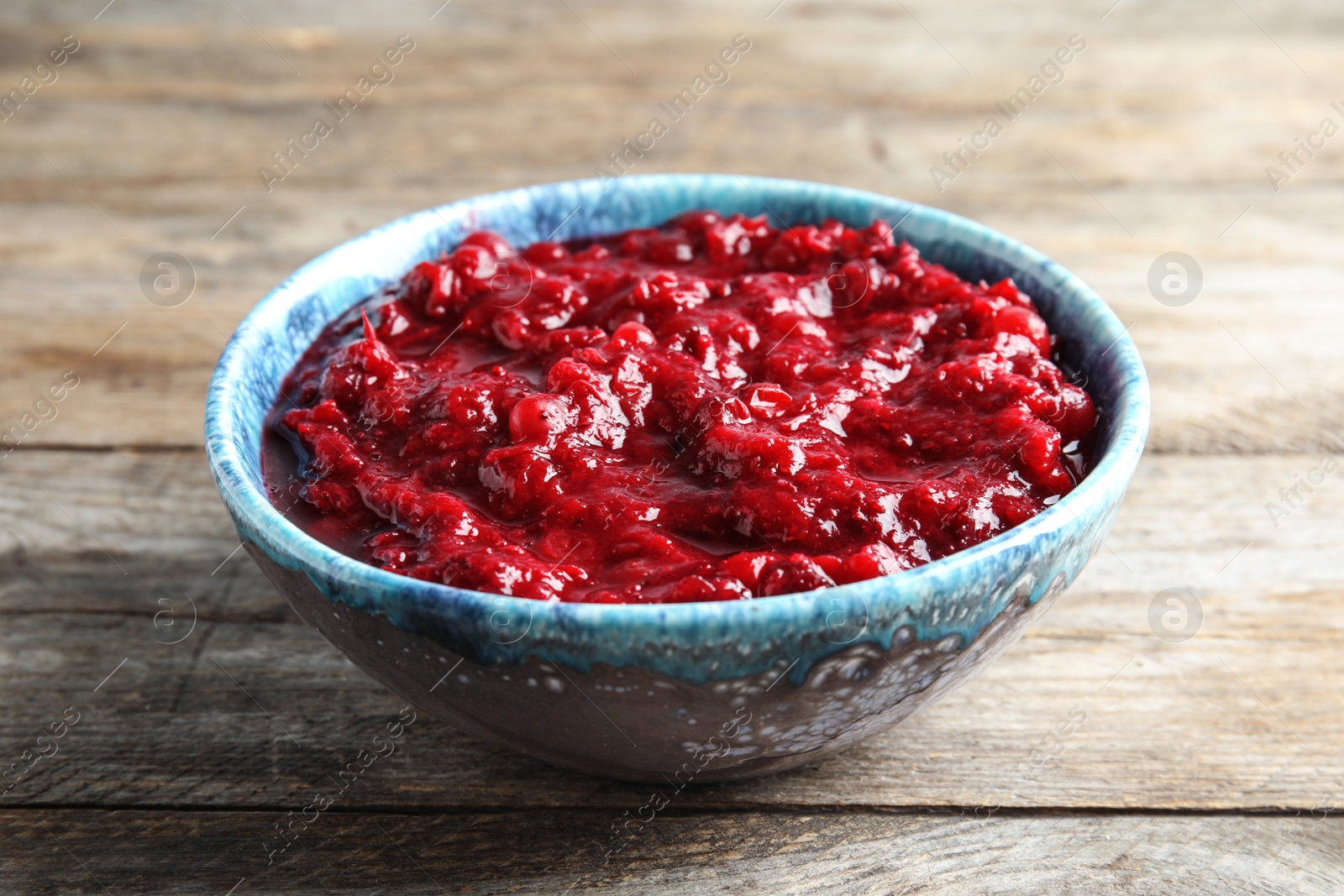 Photo of Bowl of tasty cranberry sauce on wooden background