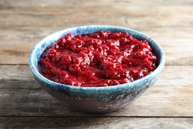 Photo of Bowl of tasty cranberry sauce on wooden background