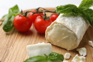 Photo of Delicious goat cheese with tomatoes and basil on wooden board, closeup