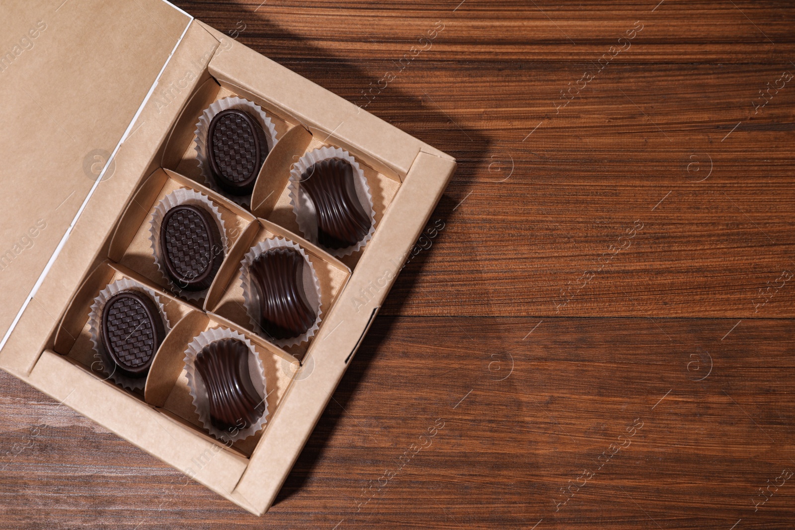 Photo of Tasty chocolate candies in box on wooden table, top view. Space for text