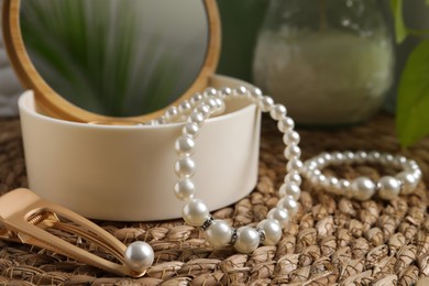 Photo of Stylish jewelry with pearls and box on wicker mat, closeup