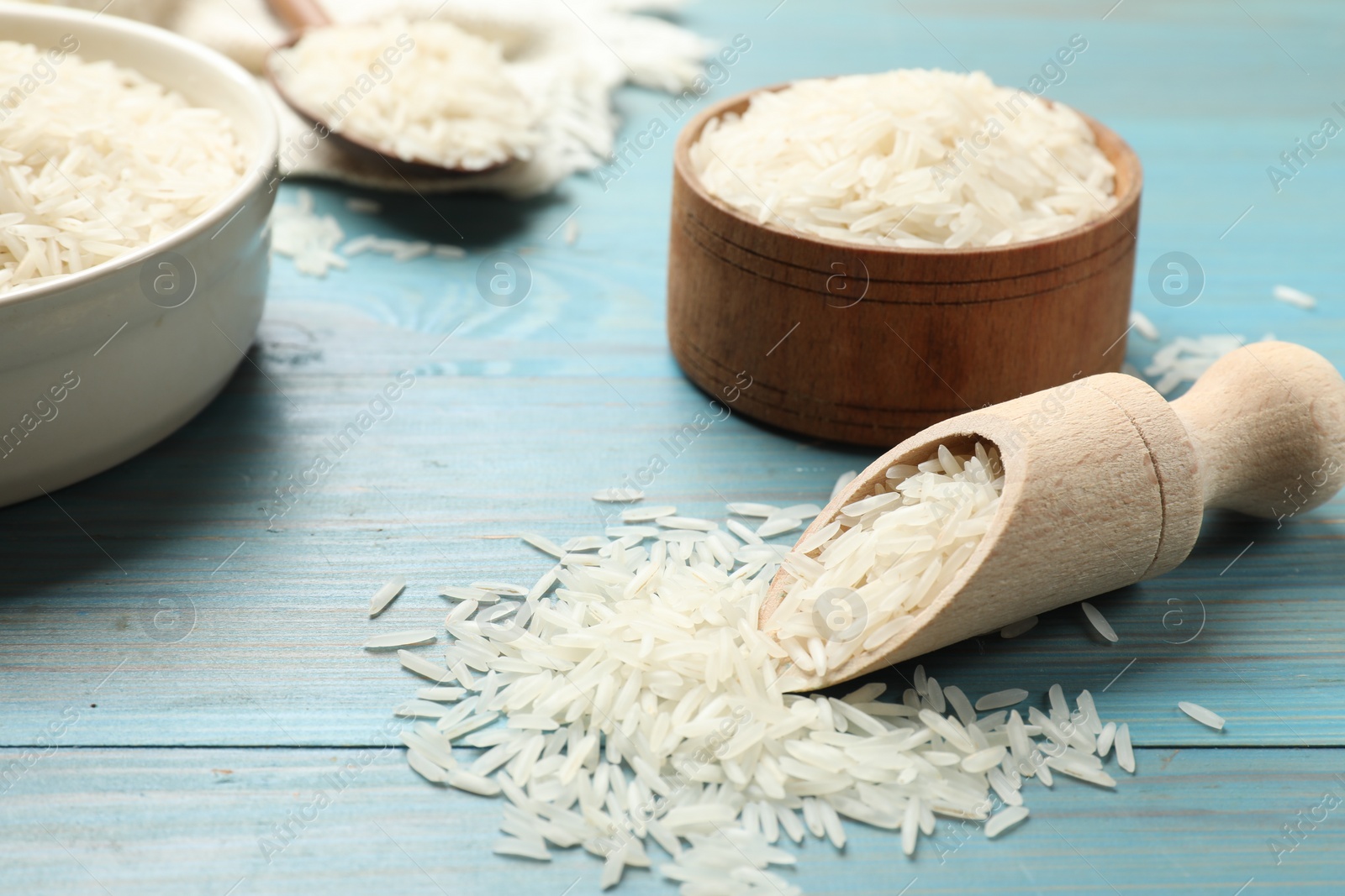 Photo of Raw basmati rice in bowls and scoop on light blue wooden table, closeup