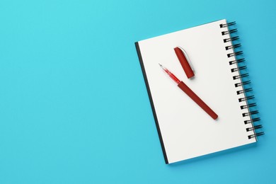 Photo of Notebook and pen on light blue background, top view. Space for text