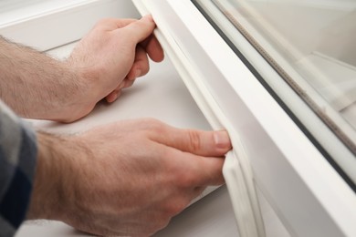 Photo of Worker putting rubber draught strip onto window indoors, closeup