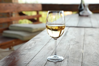 Glass of delicious white wine on wooden table in outdoor cafe, closeup