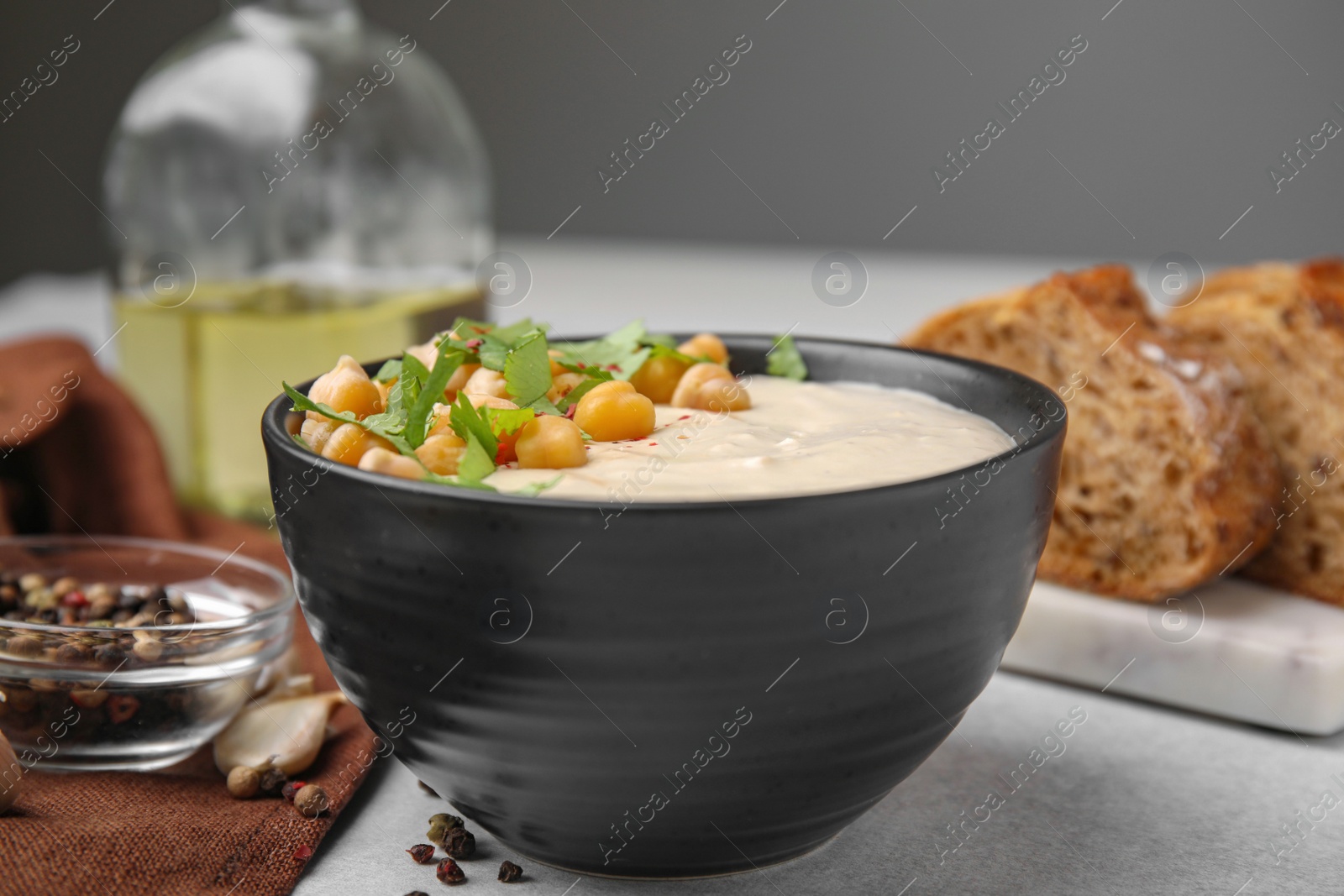 Photo of Tasty chickpea soup in bowl, bread and spices served on light grey table, closeup