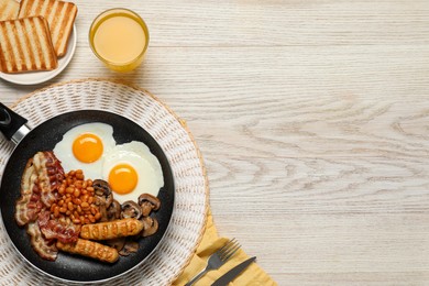 Photo of Frying pan with cooked traditional English breakfast and glass of juice on white wooden table, flat lay. Space for text