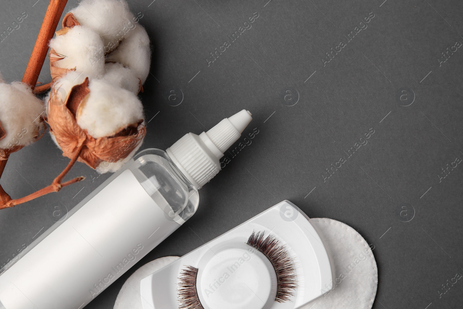 Photo of Bottle of makeup remover, cotton flowers, pads and false eyelashes on grey background, flat lay. Space for text