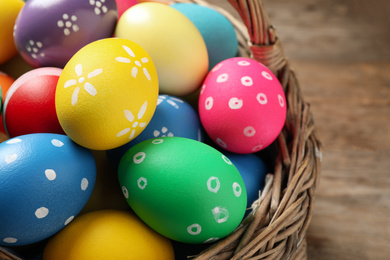 Photo of Colorful Easter eggs in basket on wooden background, closeup
