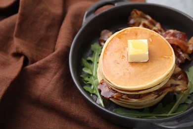 Tasty pancakes with butter, fried bacon and fresh arugula on grey table, closeup