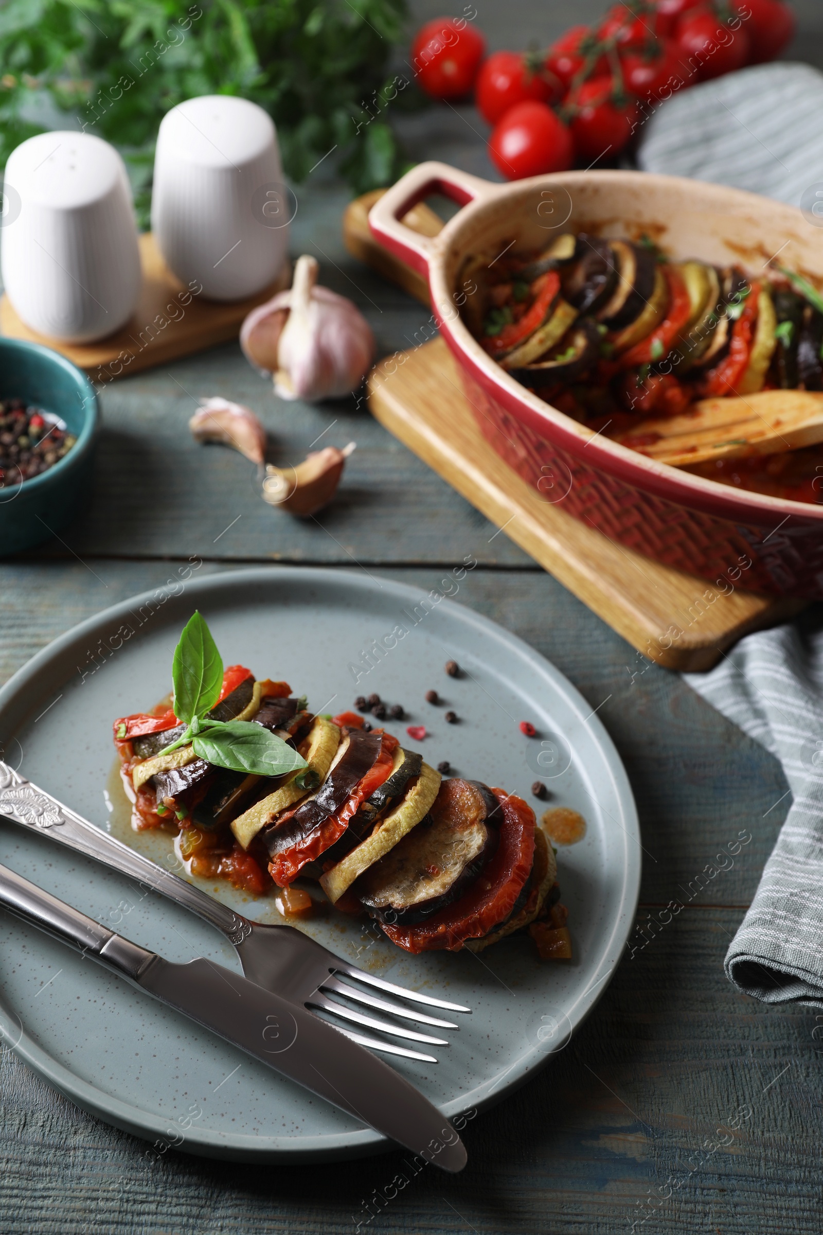 Photo of Delicious ratatouille served with basil on grey wooden table