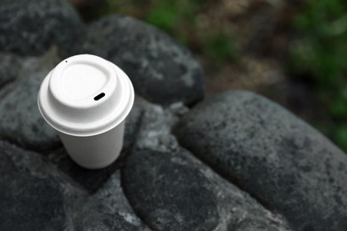 Photo of Cardboard takeaway coffee cup with lid on stones outdoors, above view. Space for text