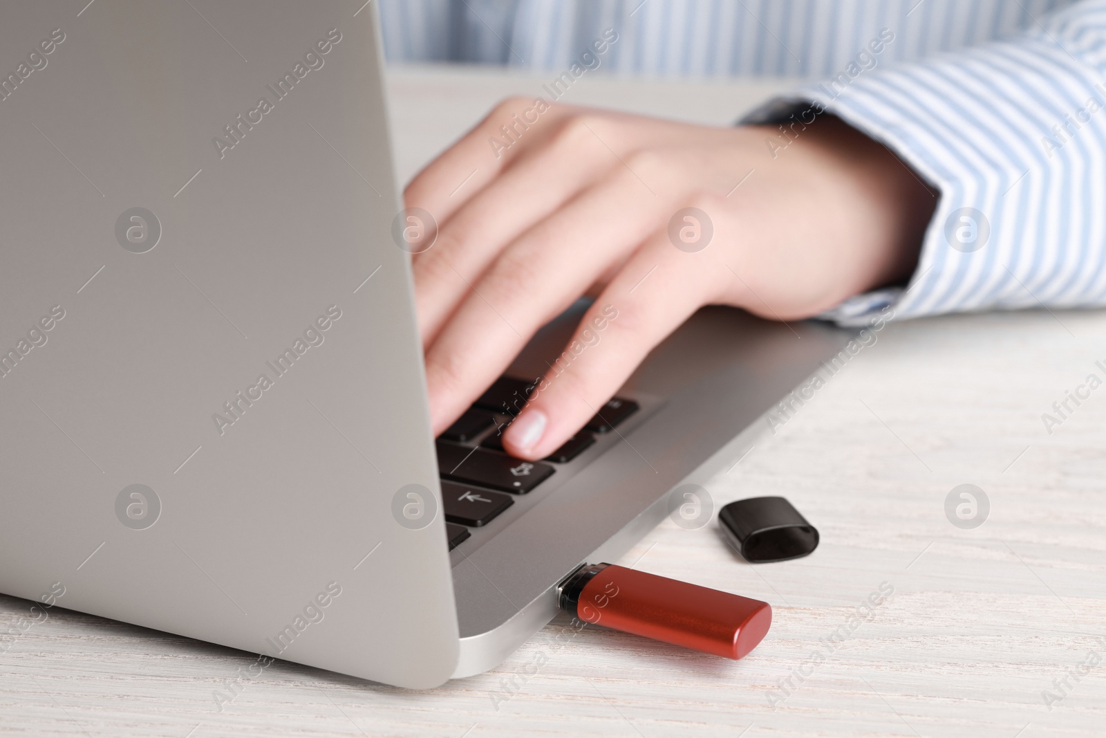 Photo of Woman using laptop with attached usb flash drive at wooden table, closeup