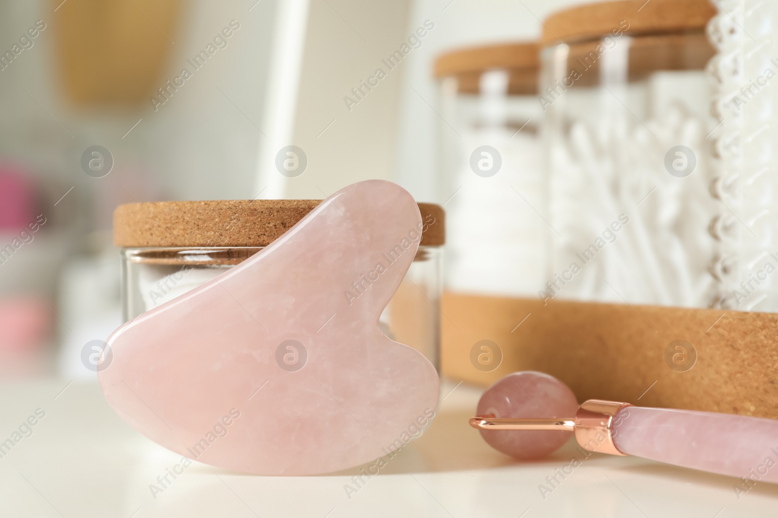 Photo of Rose quartz gua sha tool, natural face roller and toiletries on white shelf, closeup