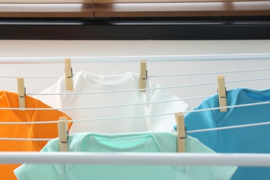 Photo of Different cute baby onesies hanging on clothes line indoors. Laundry day