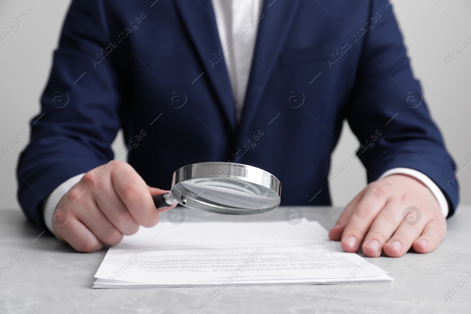 Photo of Man looking at document through magnifier at light grey table, closeup. Searching concept