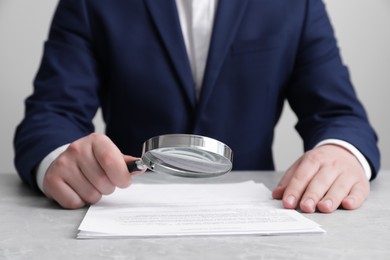 Man looking at document through magnifier at light grey table, closeup. Searching concept