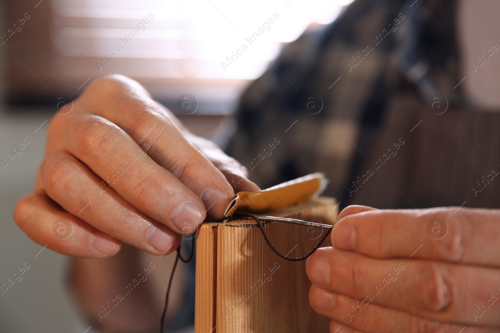 Photo of Man sewing piece of leather in workshop, closeup