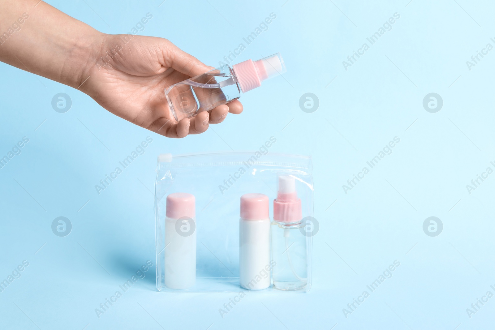 Photo of Cosmetic travel kit. Woman putting small bottle with personal care product into plastic bag against light blue background, closeup. Space for text