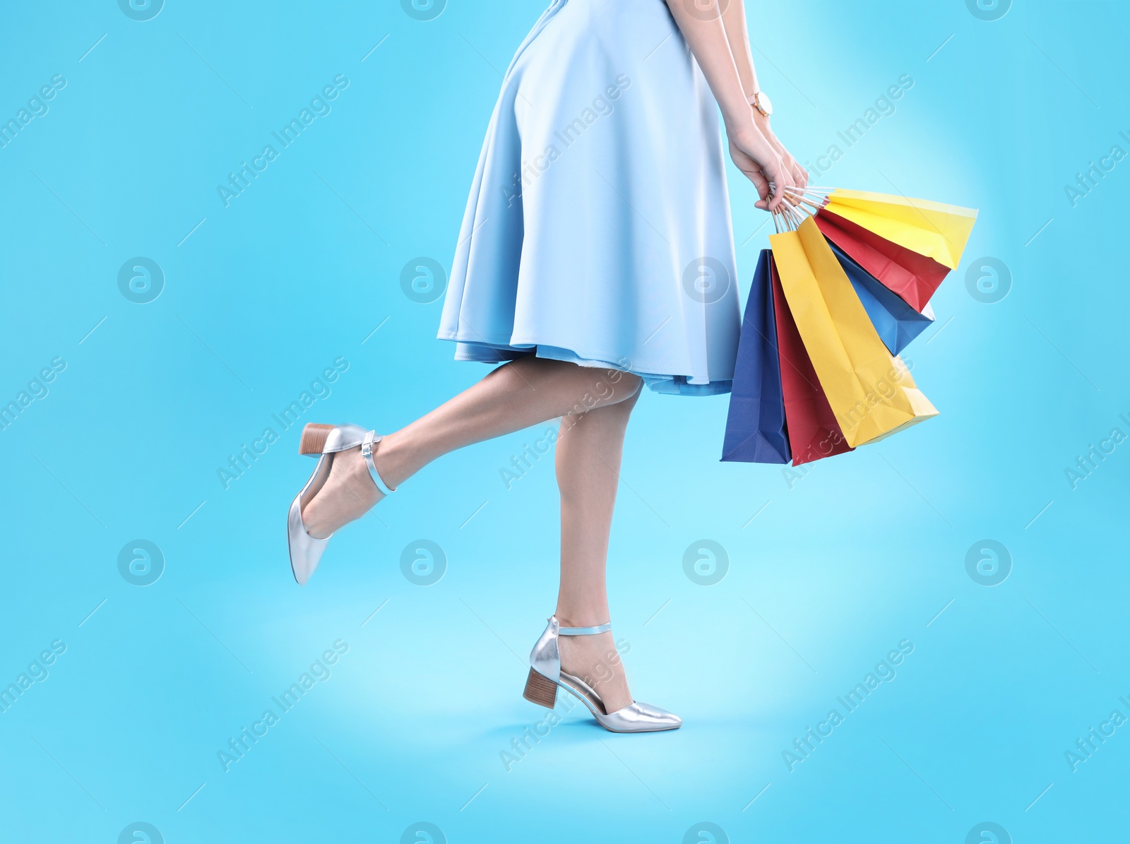 Photo of Young woman with shopping bags on color background, closeup of legs