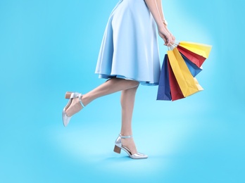 Photo of Young woman with shopping bags on color background, closeup of legs