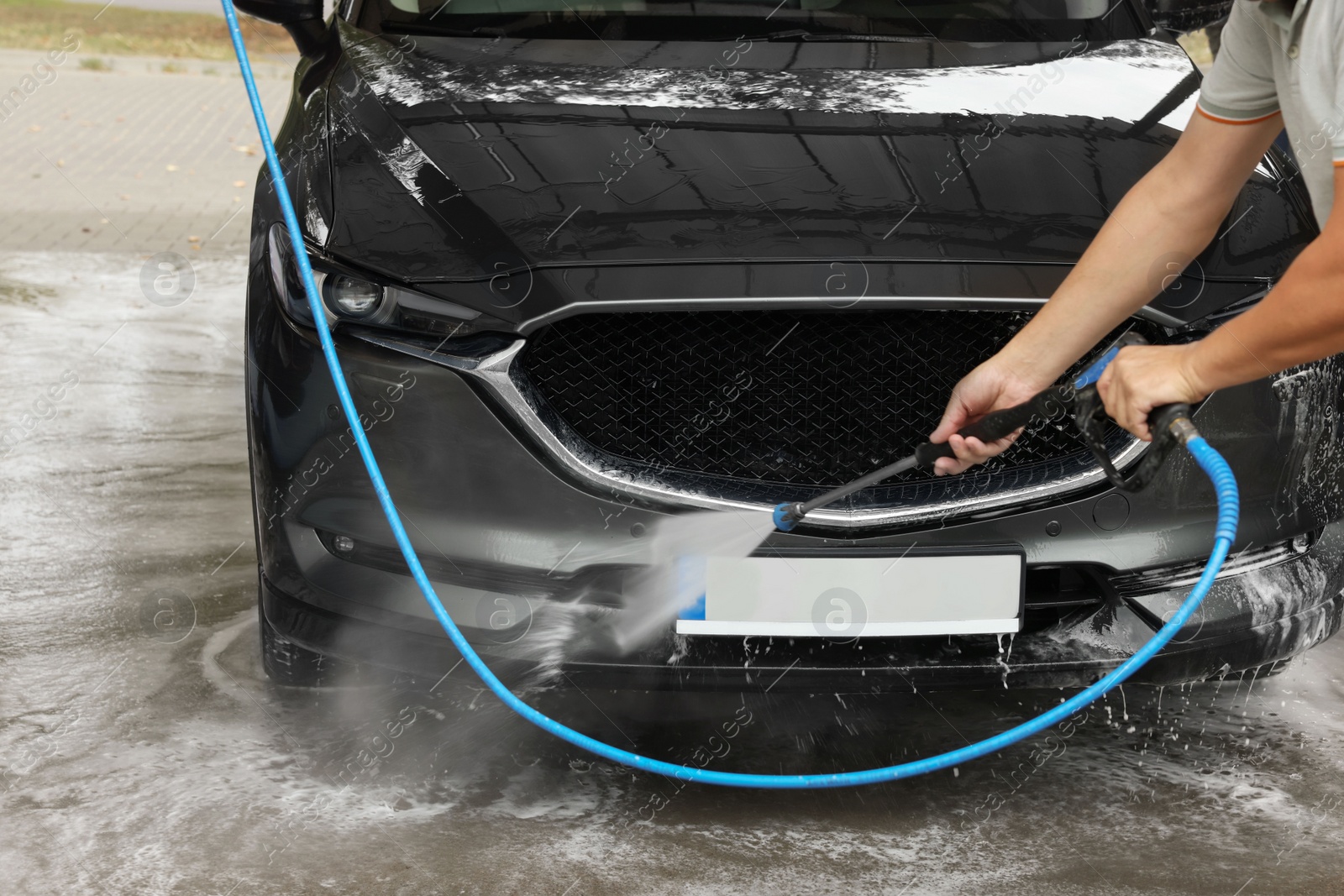 Photo of Man washing auto with high pressure water jet at car wash, closeup