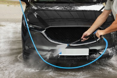 Man washing auto with high pressure water jet at car wash, closeup