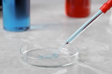 Glass pipette and petri dish with liquid on grey marble table, closeup