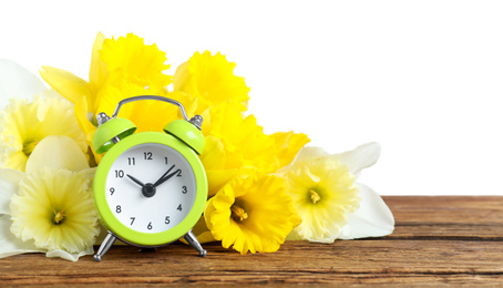 Green alarm clock and spring flowers on wooden table against white background. Time change