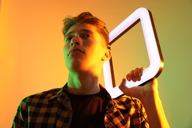 Photo of Young man with square lamp on color background in neon lights