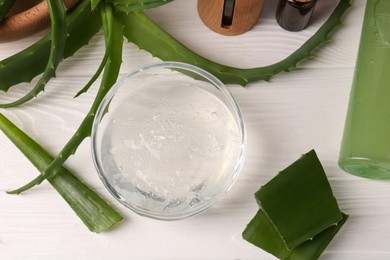Bowl of cosmetic gel and cut aloe vera leaves on white wooden table, flat lay