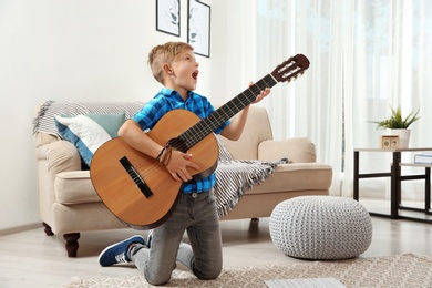 Photo of Emotional little boy playing guitar on floor in room