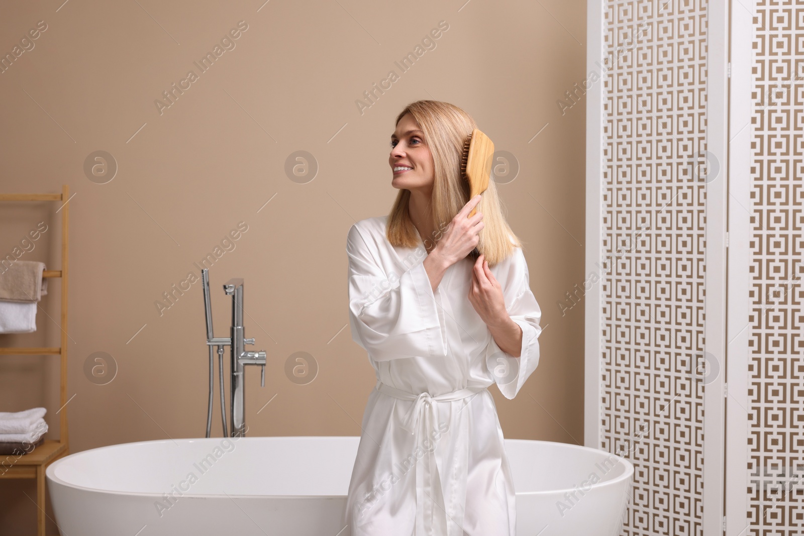 Photo of Beautiful woman brushing her hair near tub in bathroom