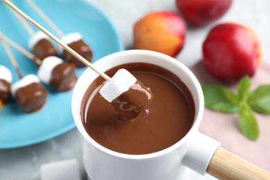 Photo of Dipping marshmallow into fondue pot with milk chocolate on light table, closeup