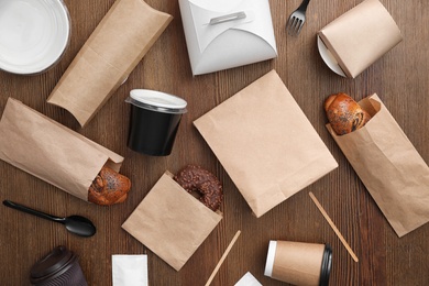 Flat lay composition with paper bags and different takeaway items on wooden background. Space for design