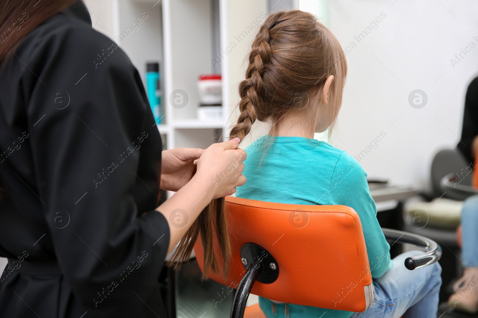 Photo of Professional female hairdresser working with little girl in salon