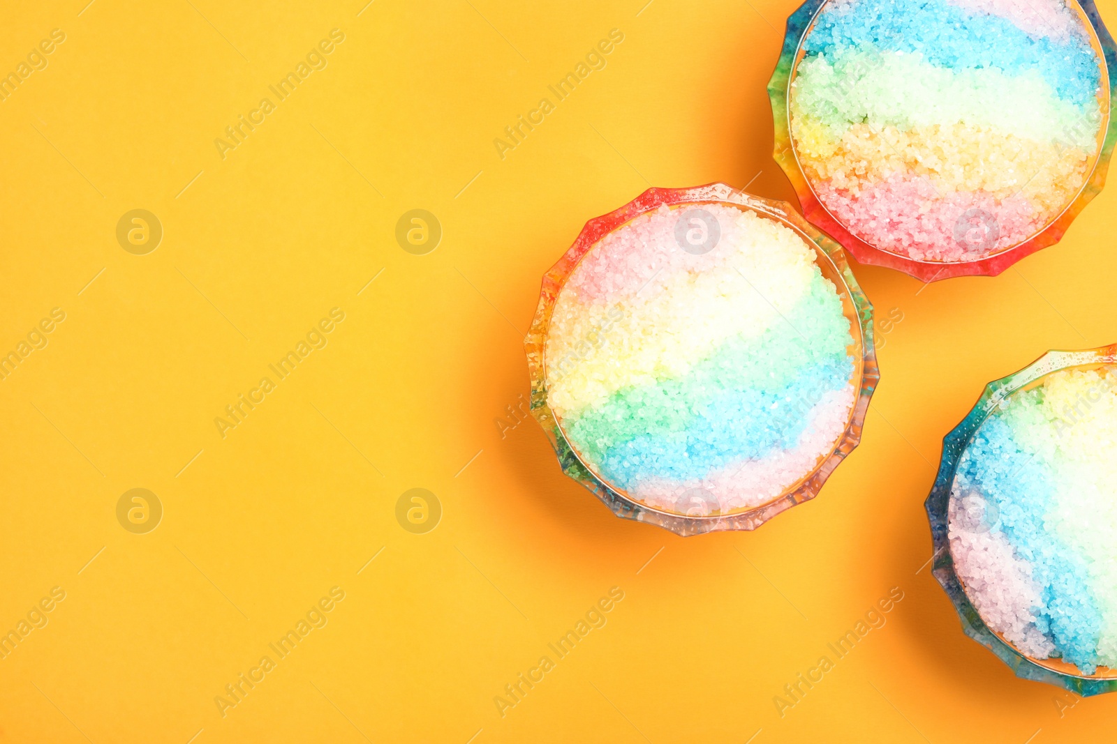 Photo of Rainbow shaving ice in glass dessert bowls on orange background, flat lay. Space for text