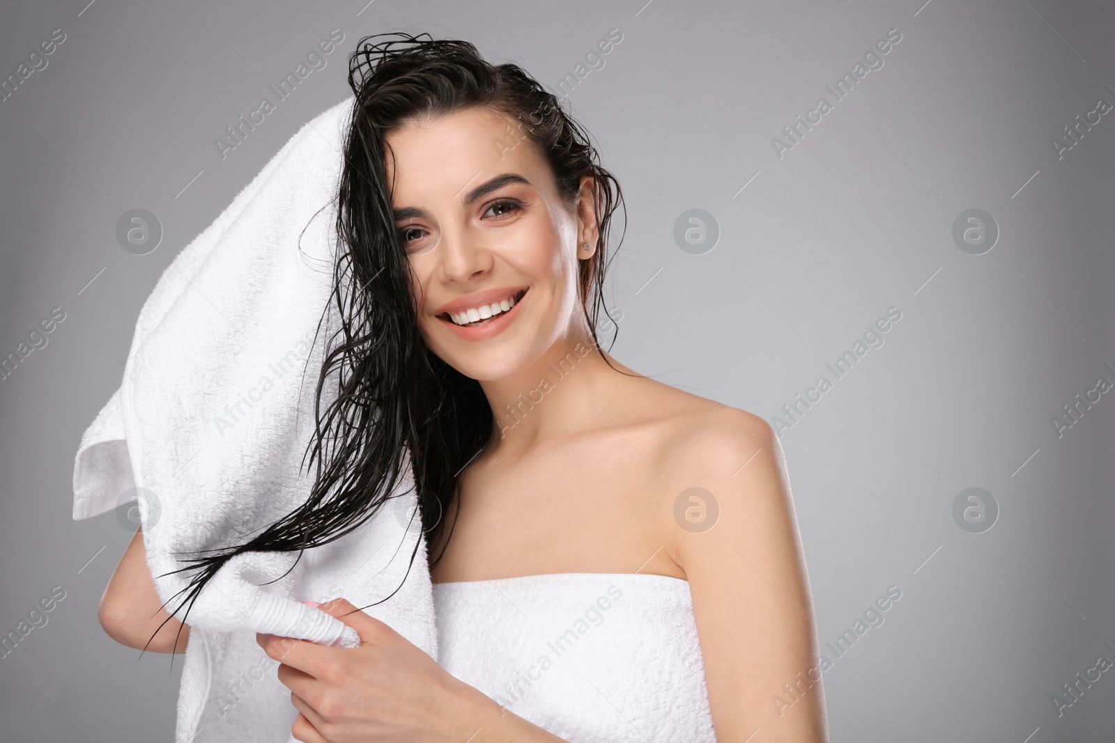 Photo of Happy young woman drying hair with towel after washing on light grey background. Space for text
