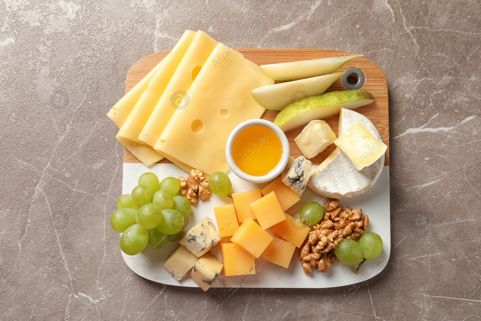 Photo of Board with different kinds of delicious cheese and snacks on marble background, top view