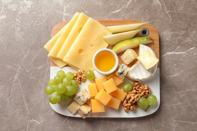 Board with different kinds of delicious cheese and snacks on marble background, top view