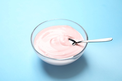 Photo of Glass bowl with creamy yogurt and spoon on color background