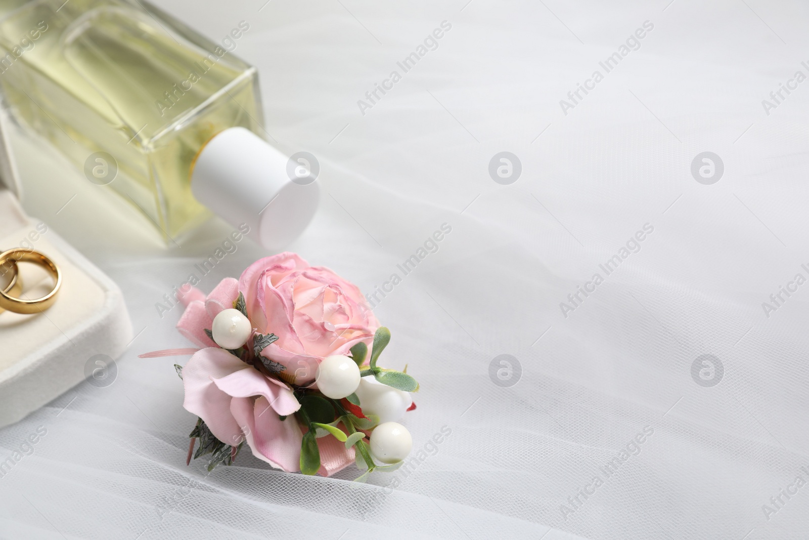 Photo of Wedding stuff. Stylish boutonniere, wedding rings and perfume bottle on white veil, closeup pace for text